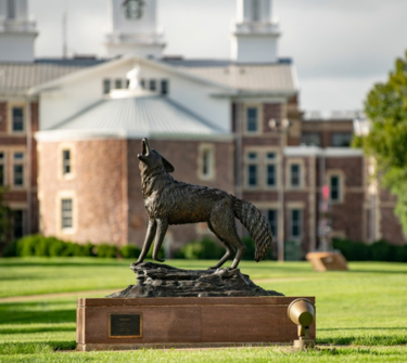 The Coyote Legacy Statue on campus with Old Main in the background.