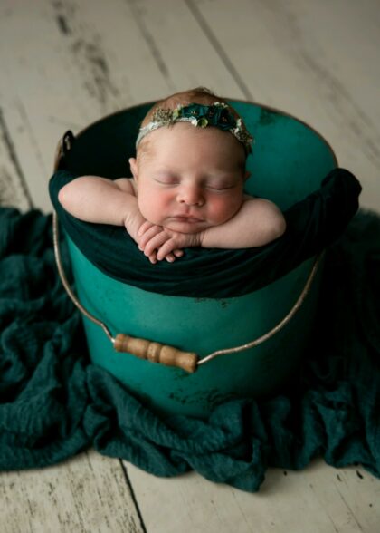 A newborn baby asleep in a green bucket.